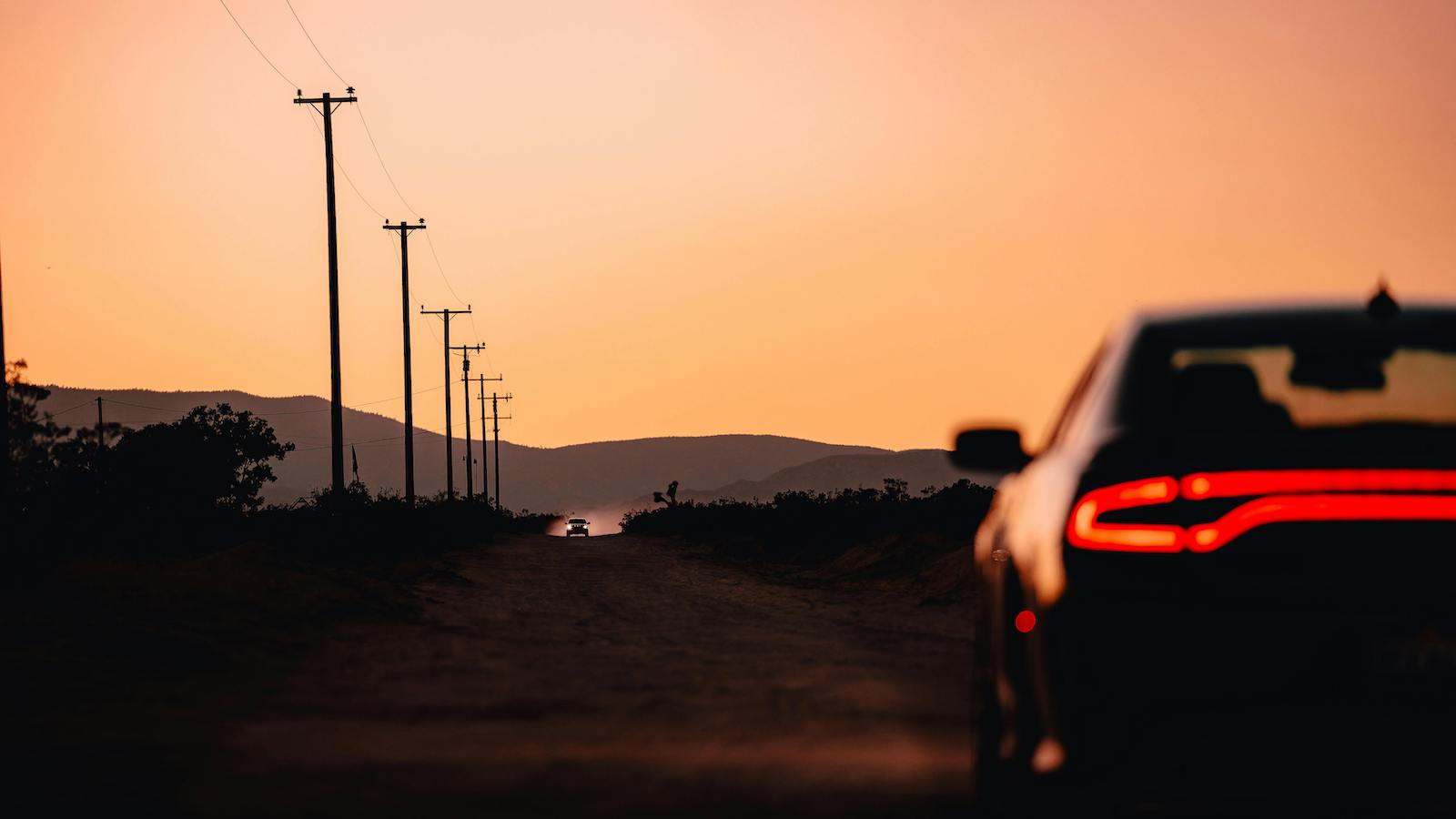 Defocused Photo of a Car on a Dirt Road with Silhouetted Mountains in Distance at Sunset
