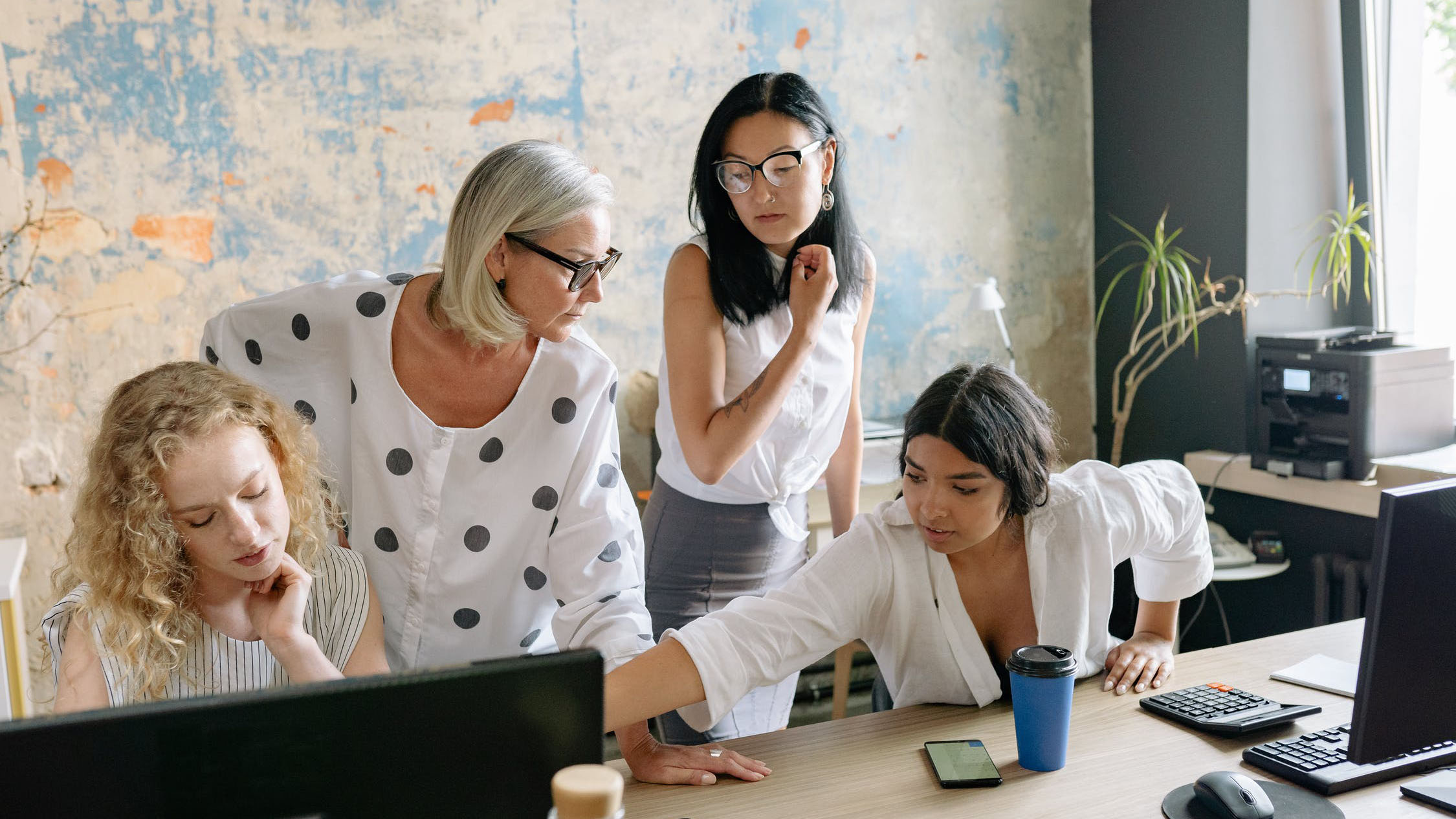 Four women in an office huddled around computers