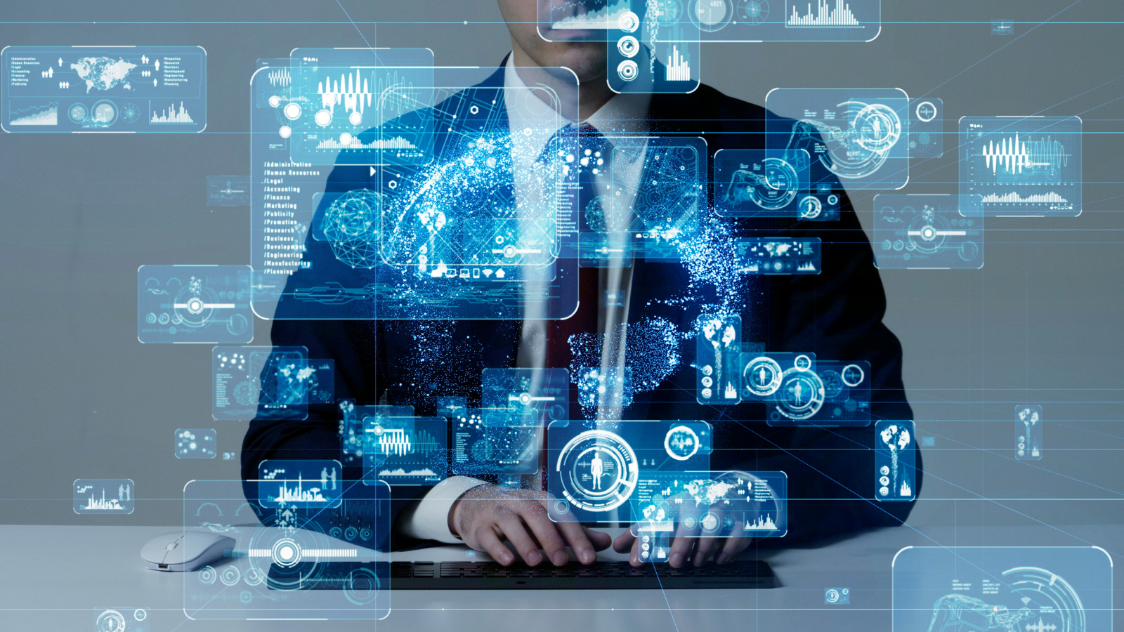 a man in a black suit, white shirt and black tie. He is sitting at a desk surrounded by graphics representing technology