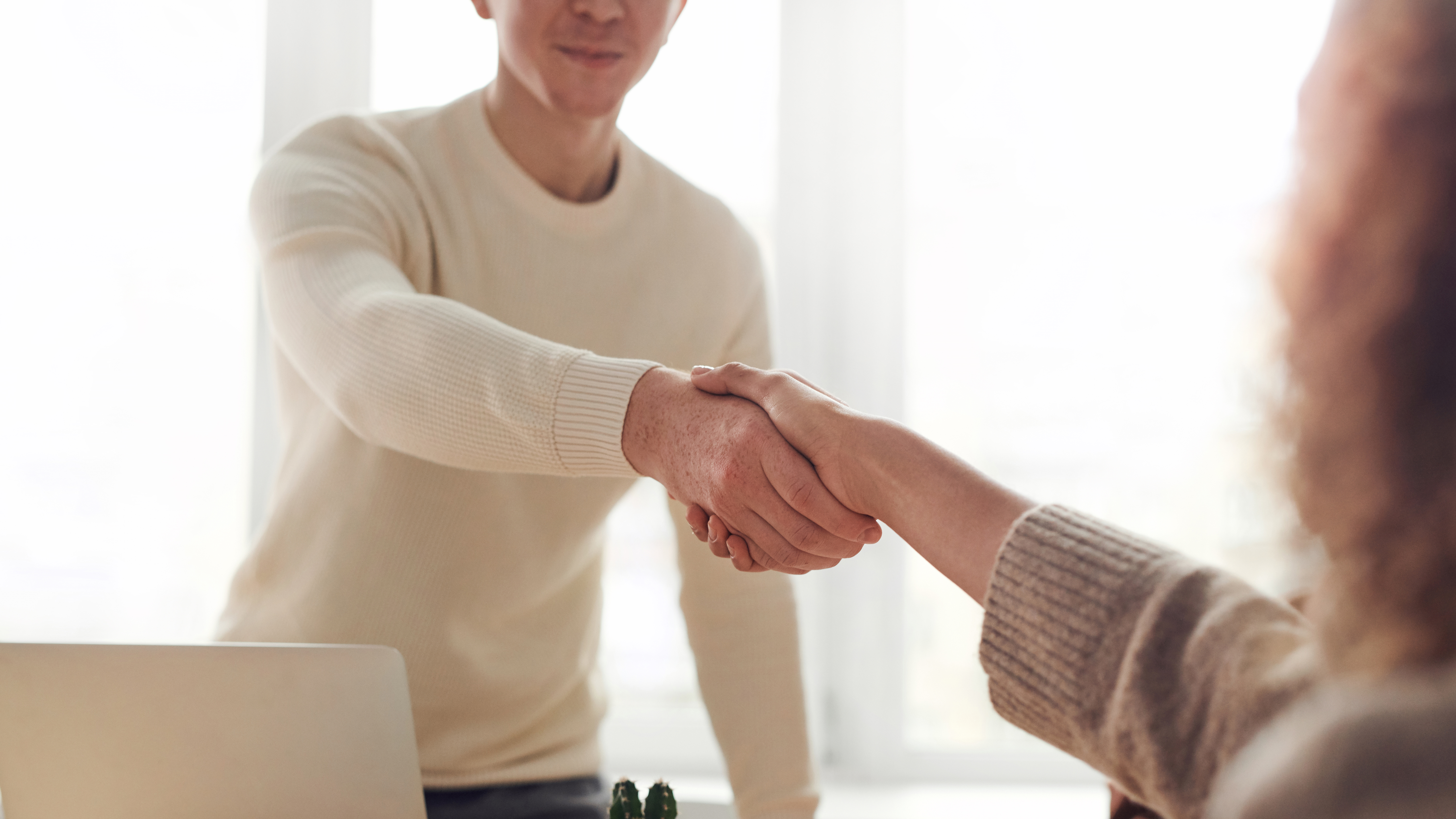 Two people shaking hands over a desk