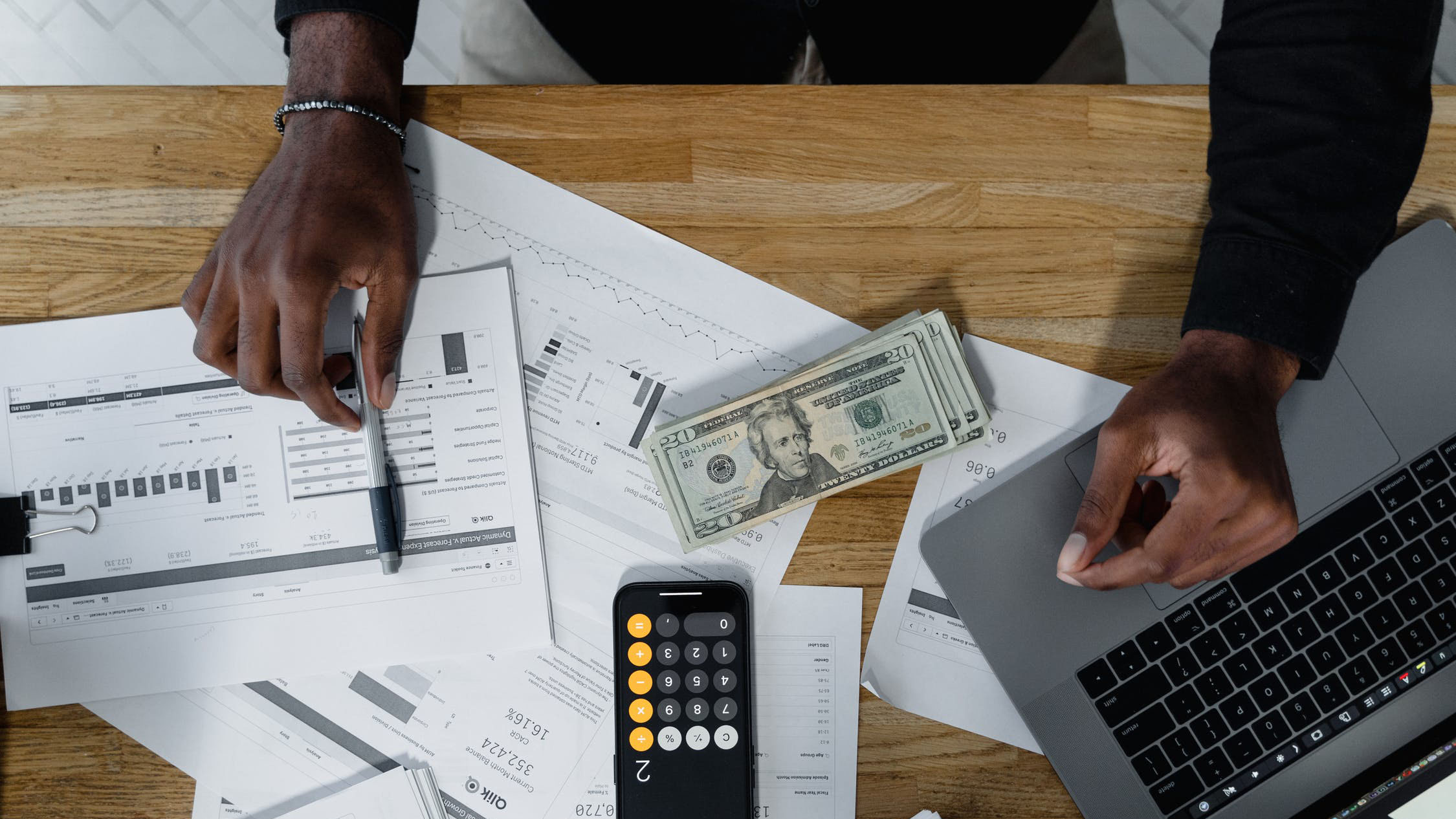 Man at a table with money, a calculator, a computer, and papers