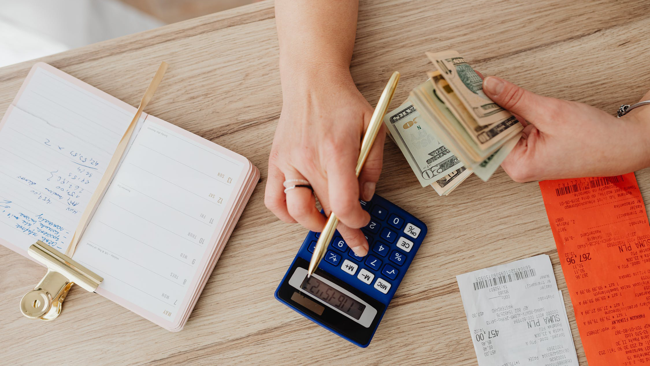 person at a desk holding a pencil and money and typing into a calculator