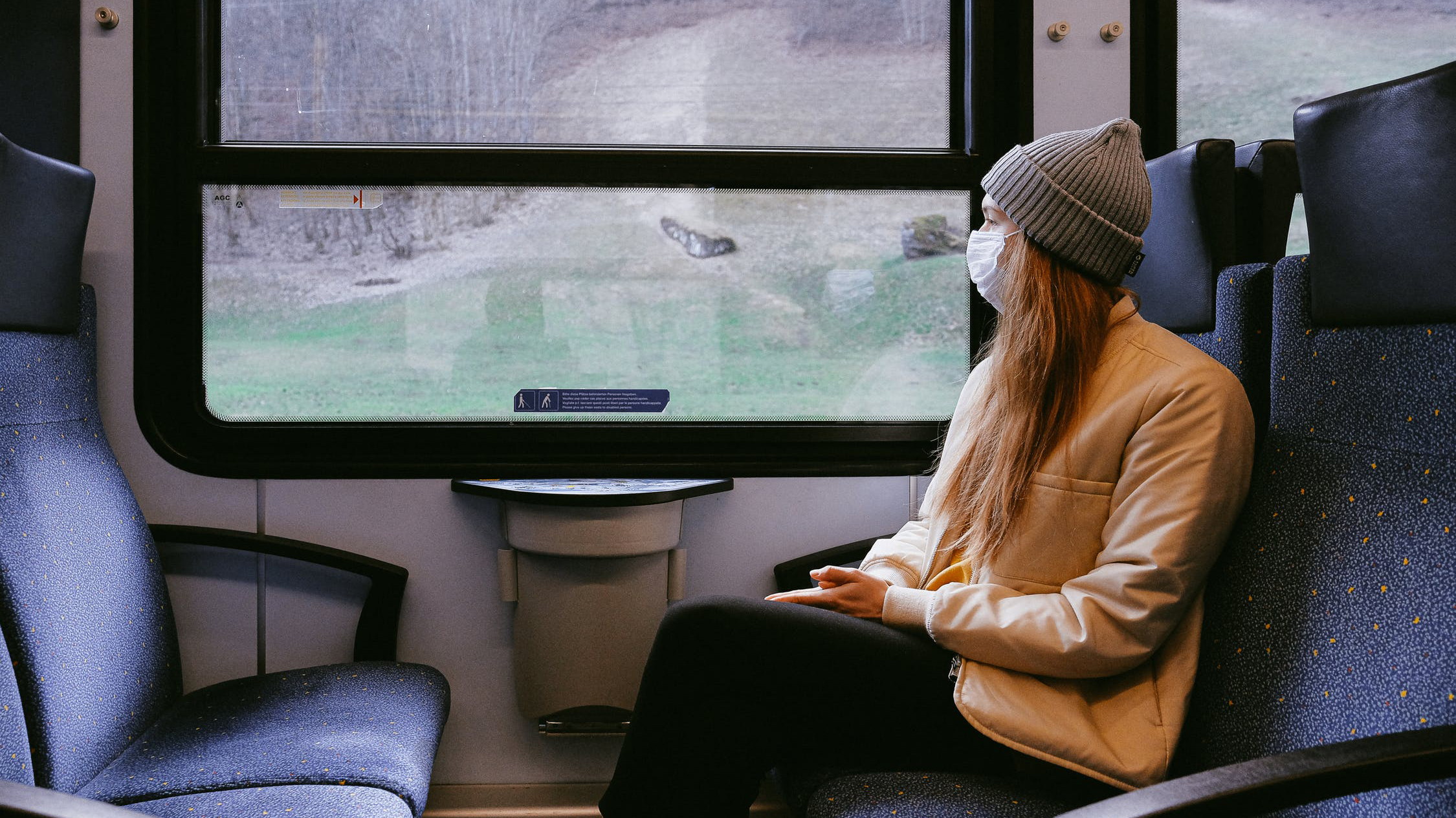 Woman wearing a mask sitting on a train and looking out the window