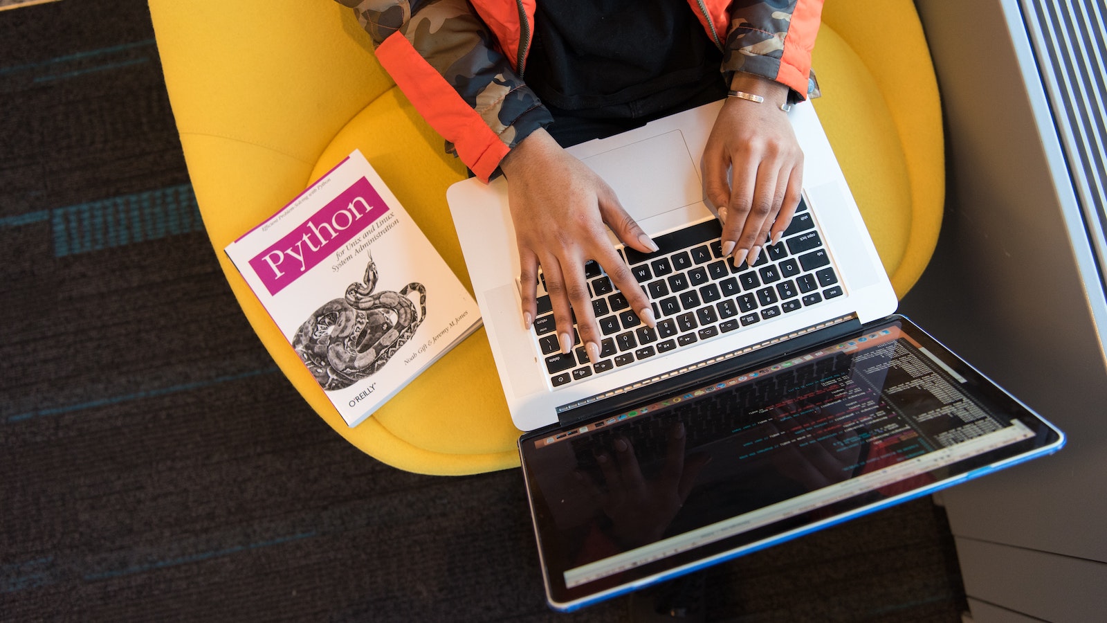 Person writing code on a computer with a book titled "Python" beside them.