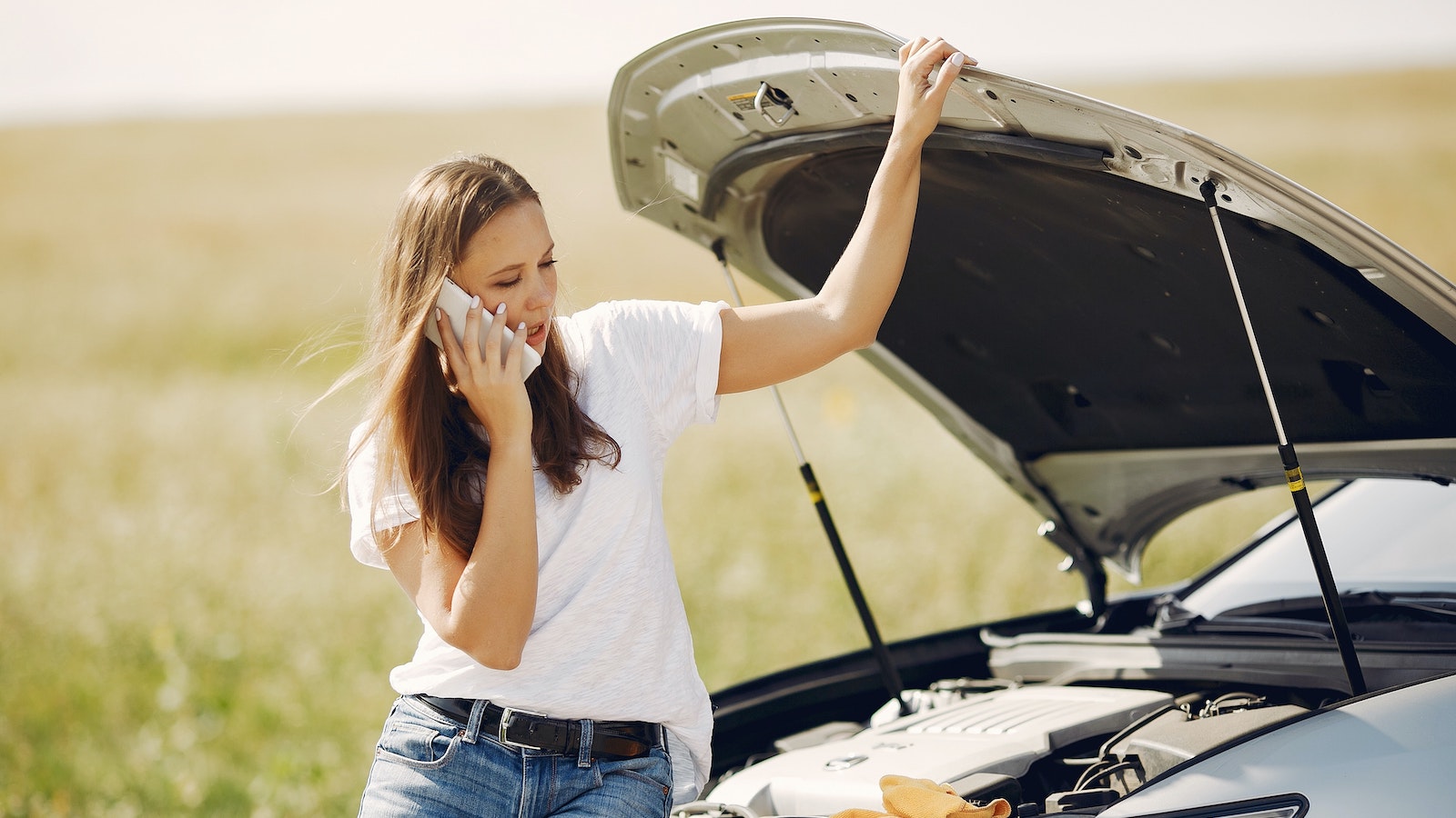 Woman calling on the phone next to the open hood of a car