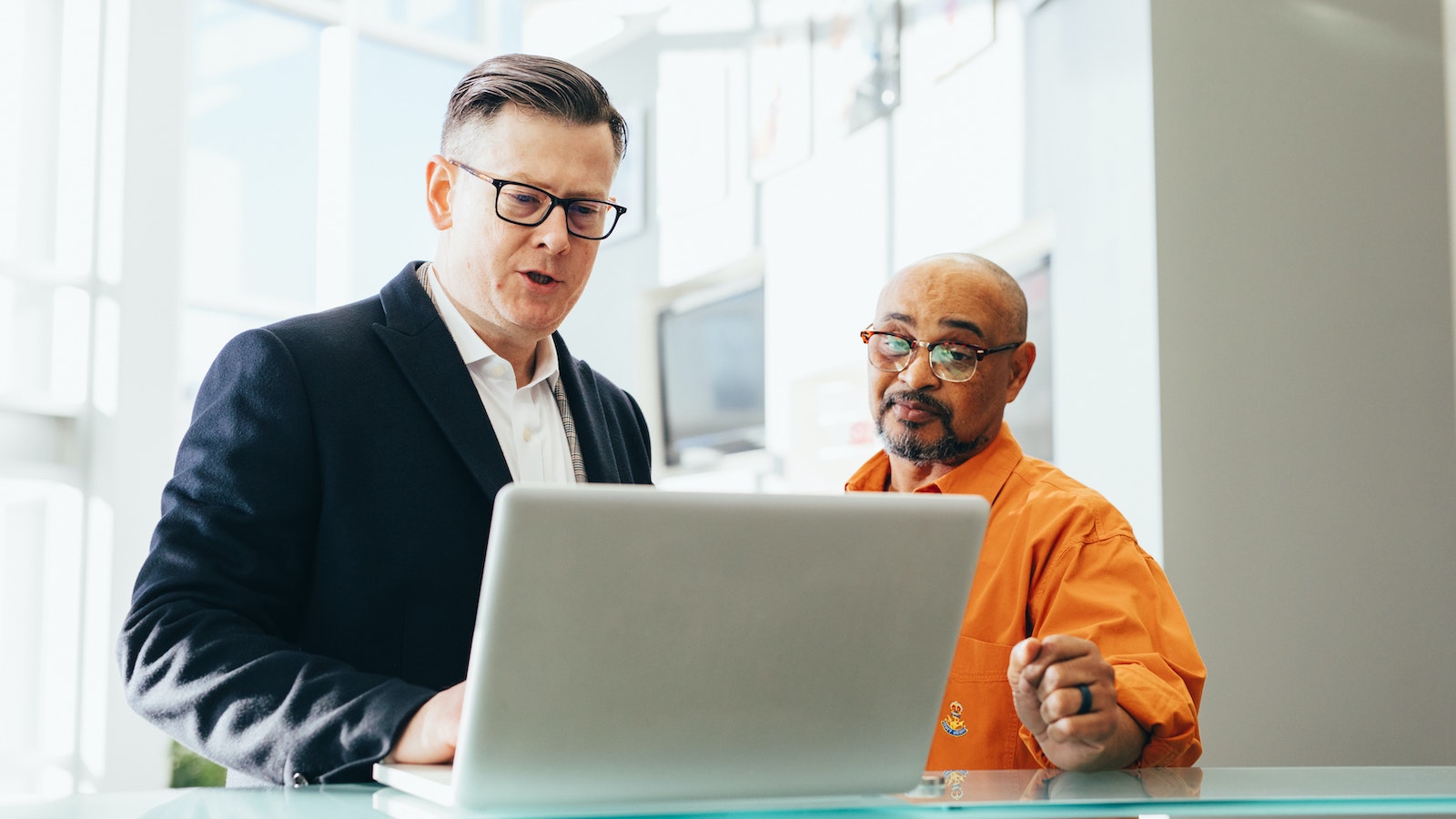 Man using a silver laptop next to another man