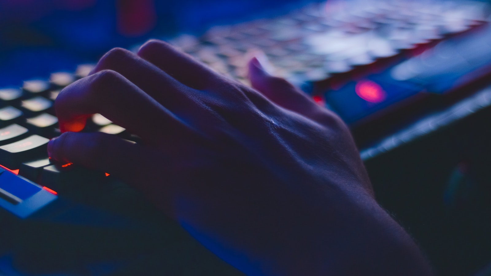 Hand typing on a colorful but dark keyboard