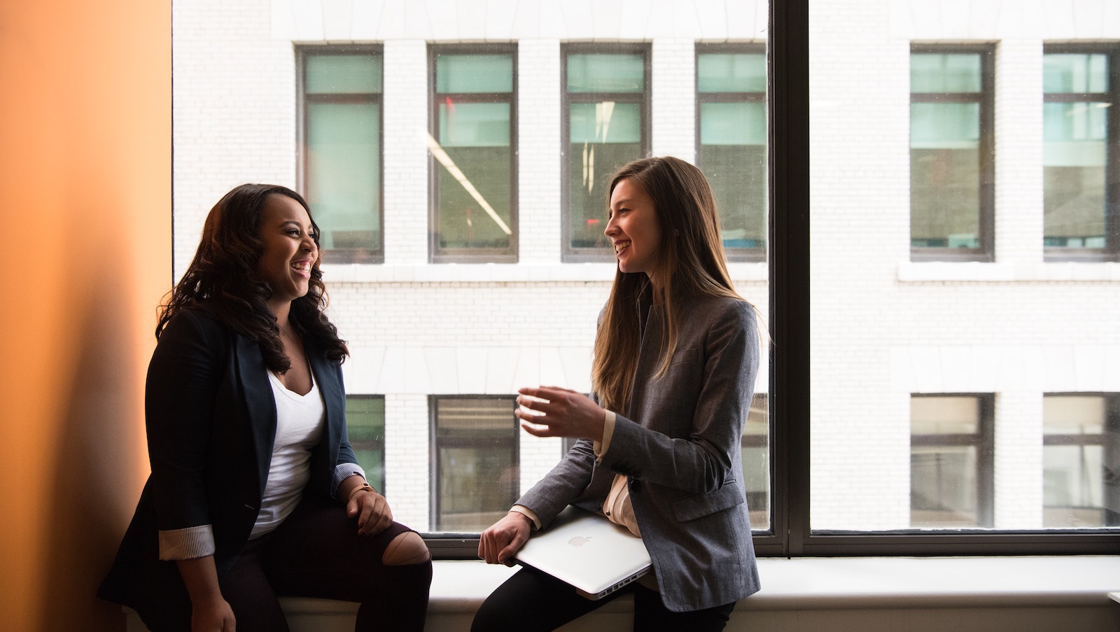 Two women chatting by a large window