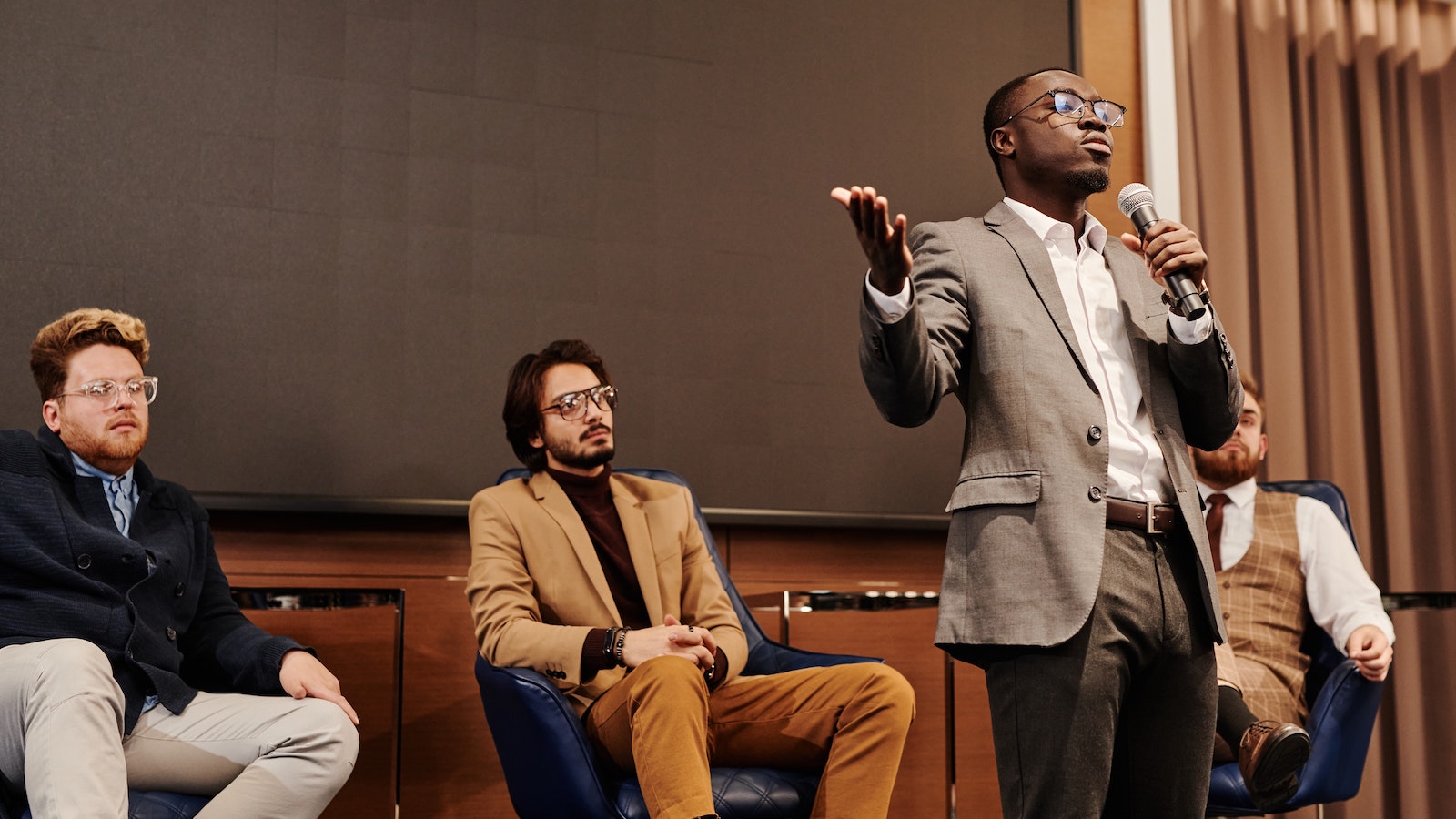 Person holding a microphone standing in front of a panel of speakers