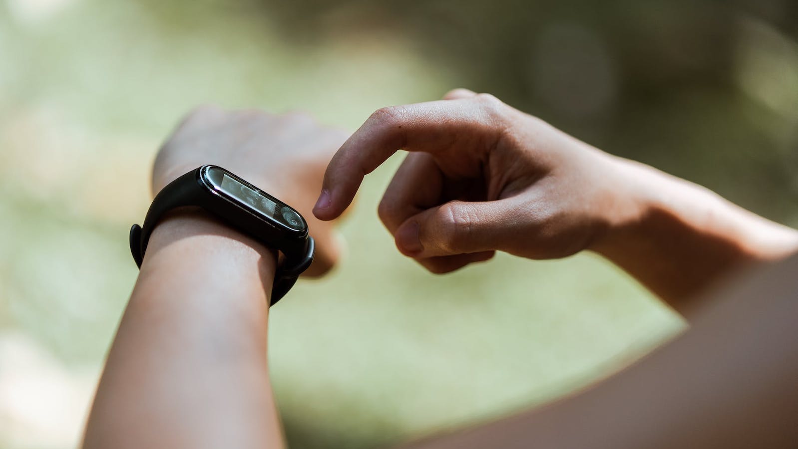 Person tapping the screen of a FitBit while outdoors