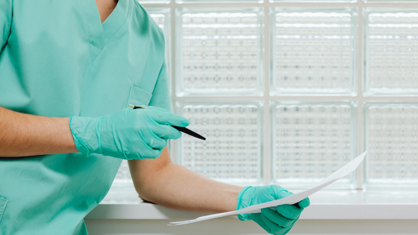 Person in gloves and hospital scrubs with a pen and paper