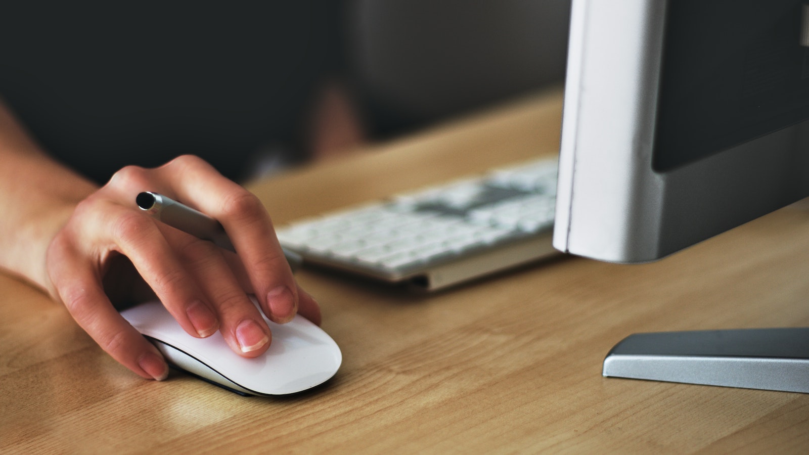 Person holding a pen in their hand while using a computer mouse