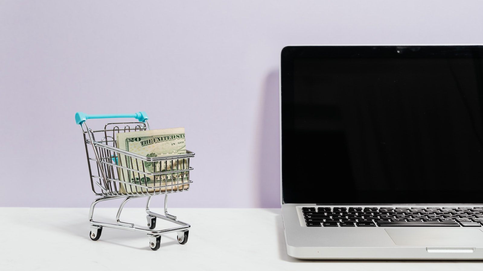 Small shopping cart with money in it next to a laptop
