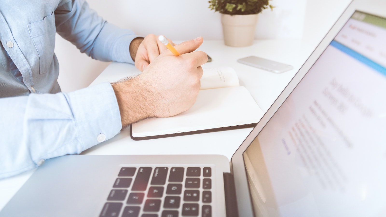 Person holding pen and notebook sitting by a computer