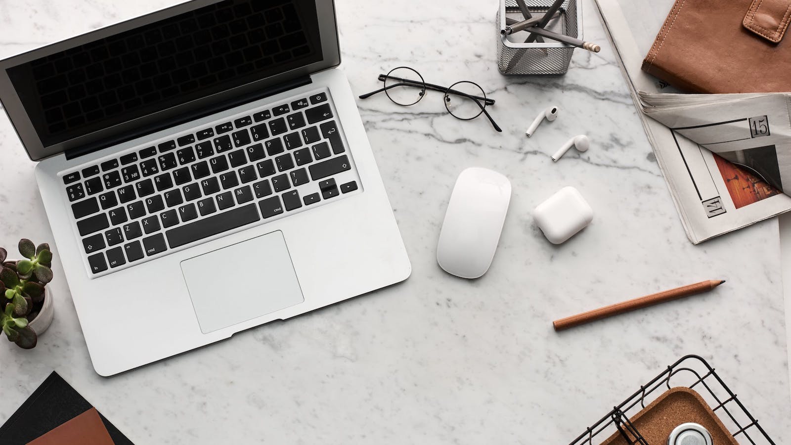 Computer on a table along with glasses, headphones, and a book