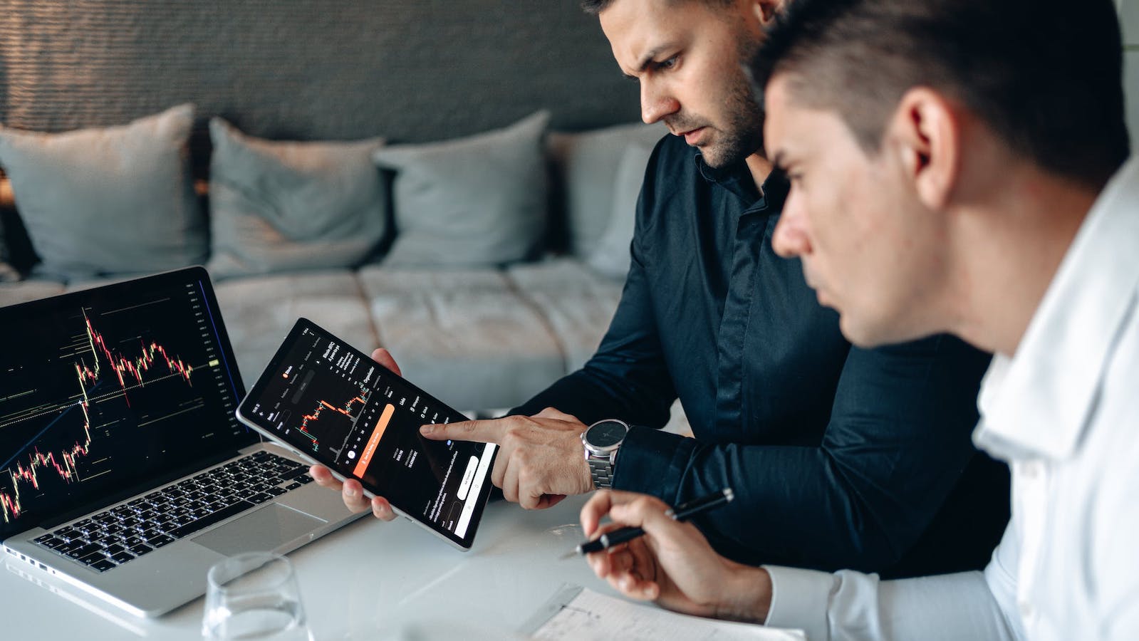 Two people sitting around a computer and tablet showing trends