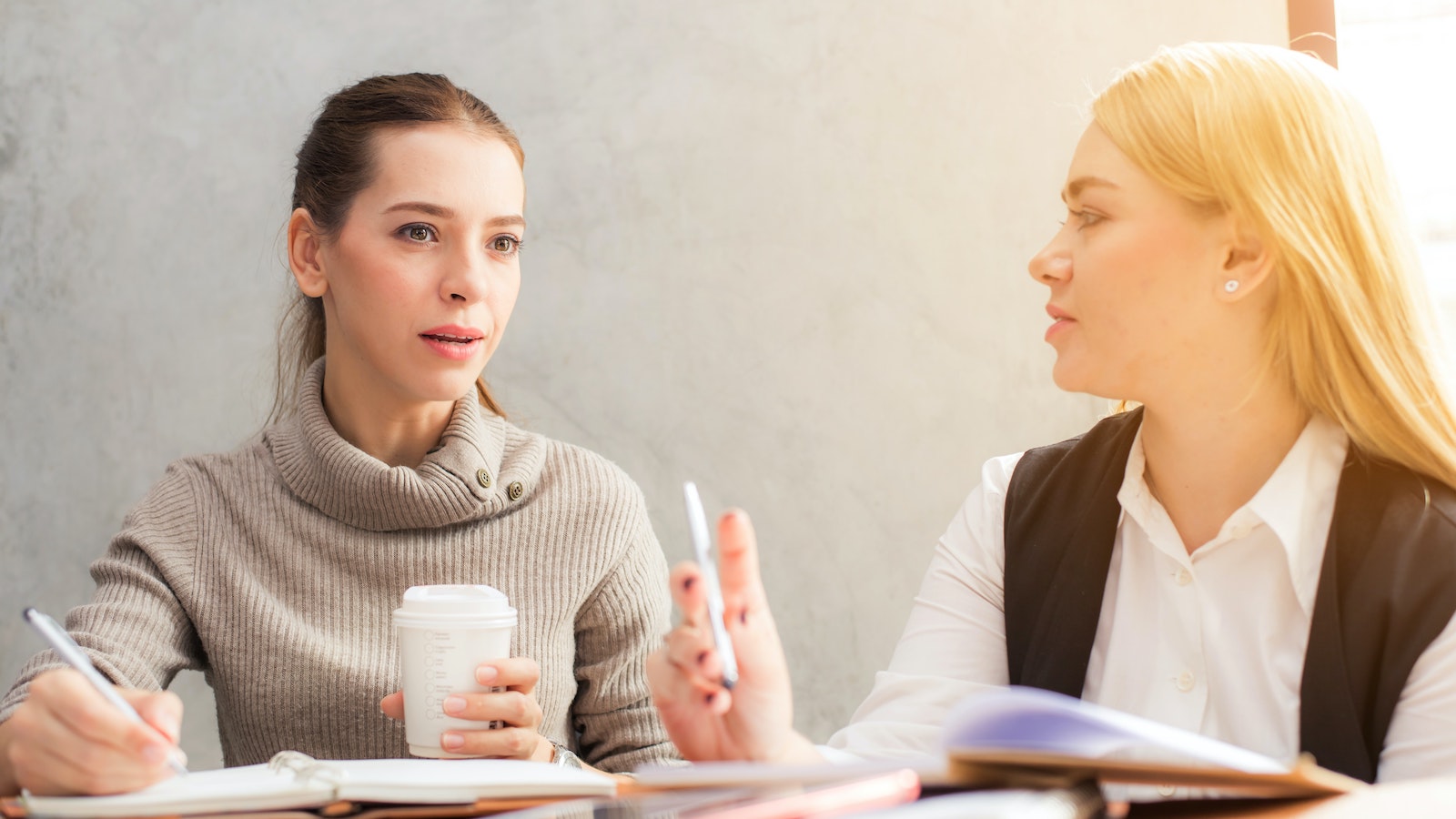 Two women sitting at a desk with notebooks