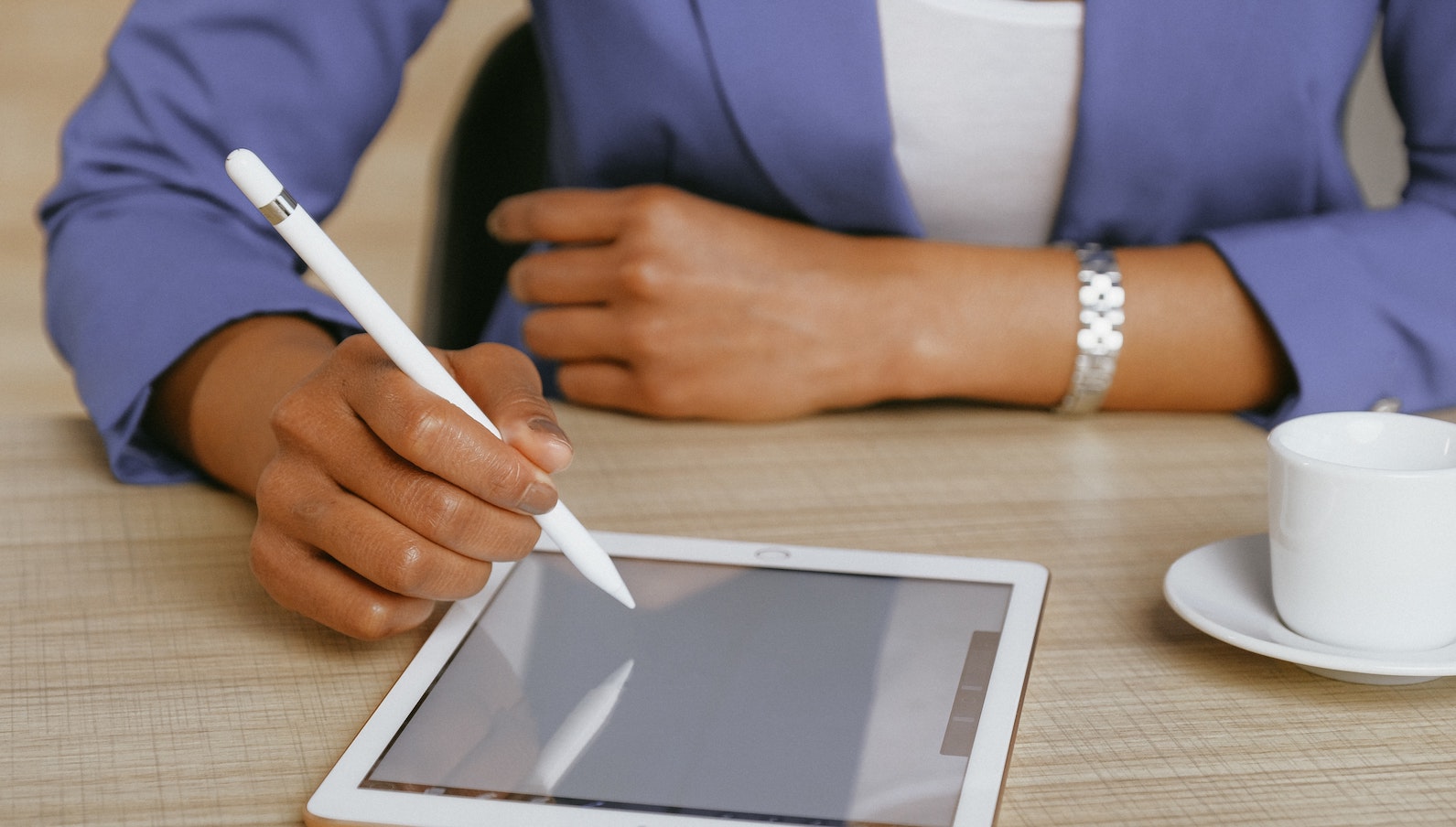 Person in a blue blazer sitting and working on a tablet