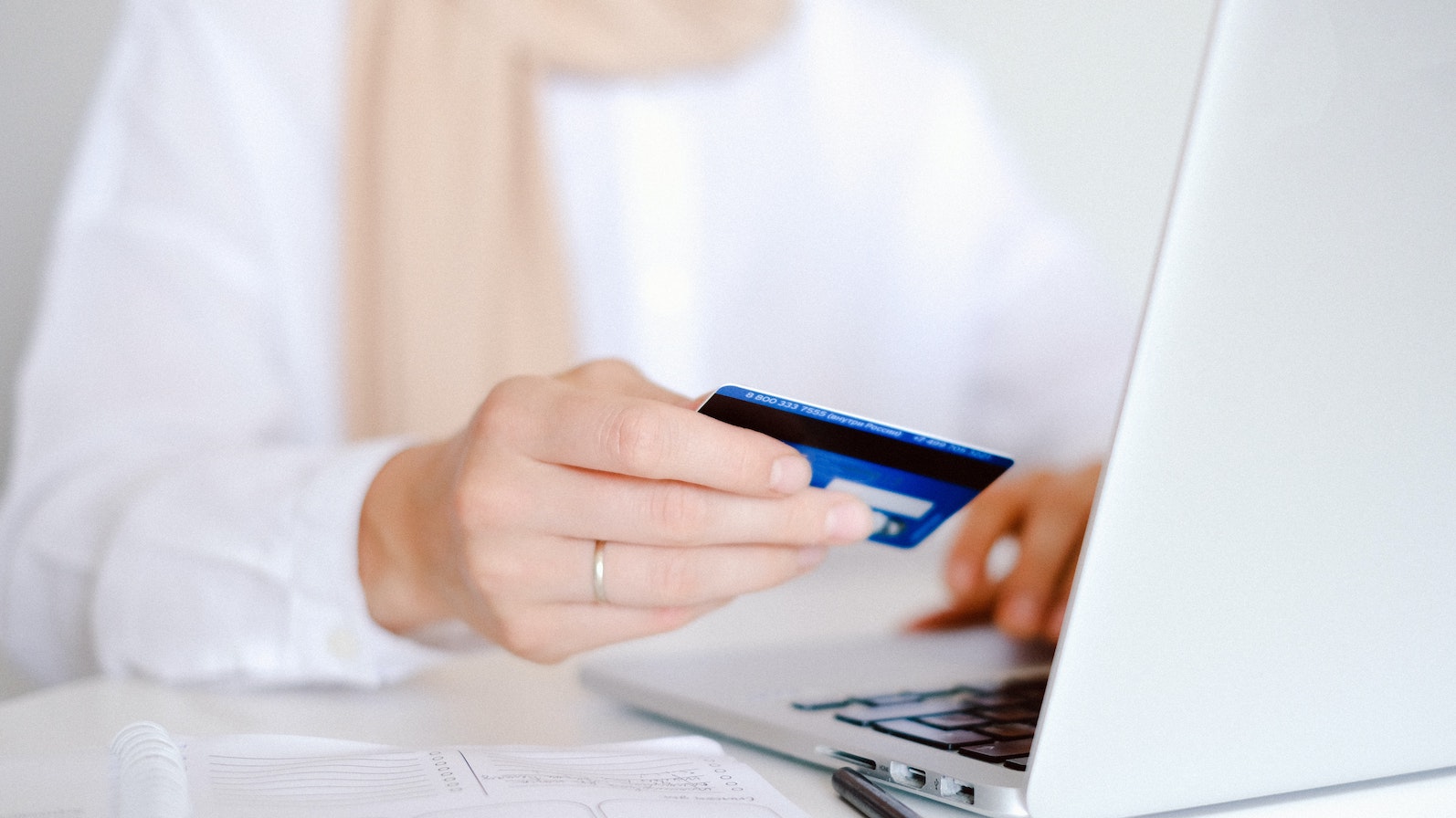 Person wearing a scarf and holding a credit card in front of a laptop