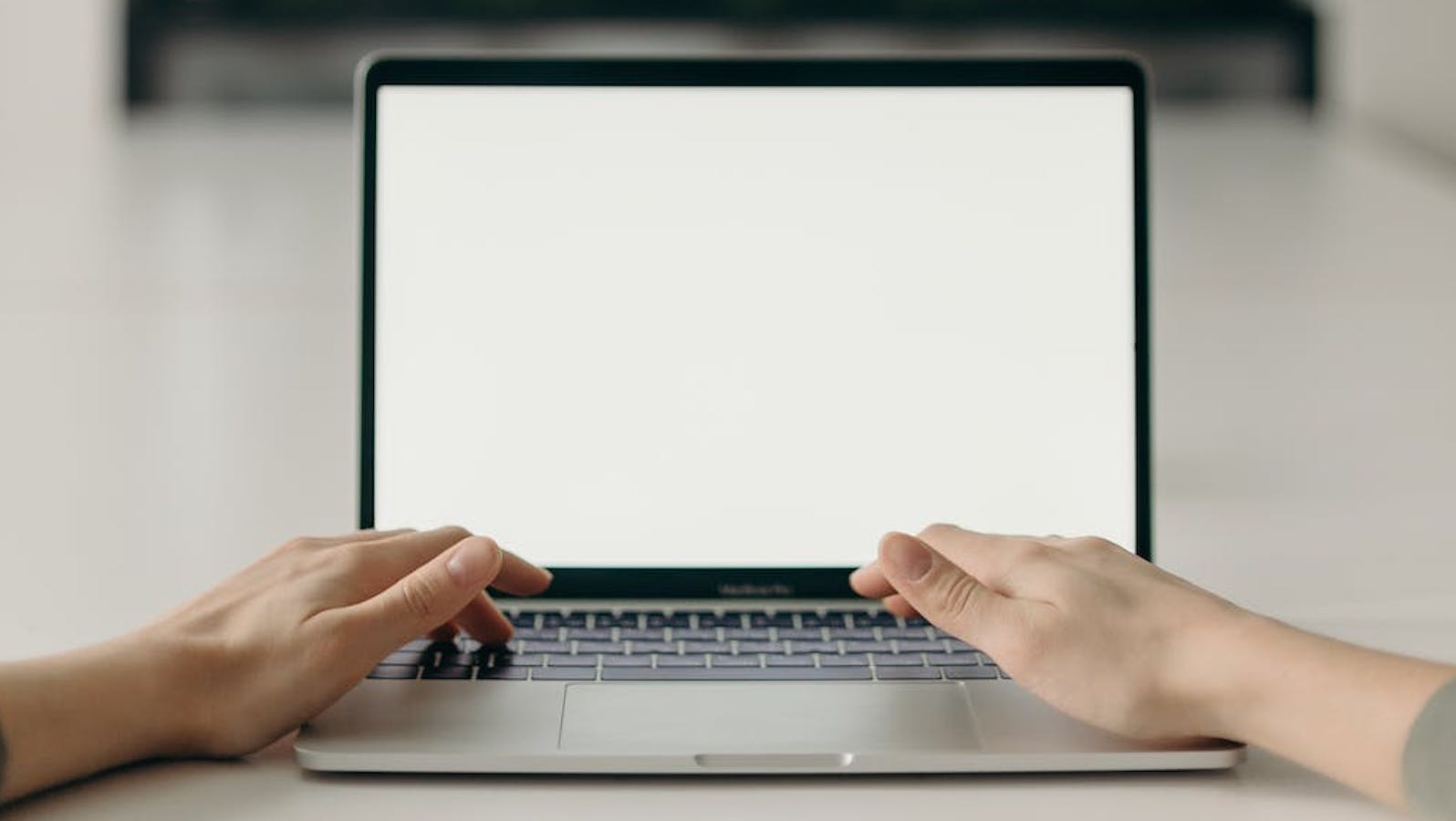 A person typing on a mac laptop where the screen is entirely white