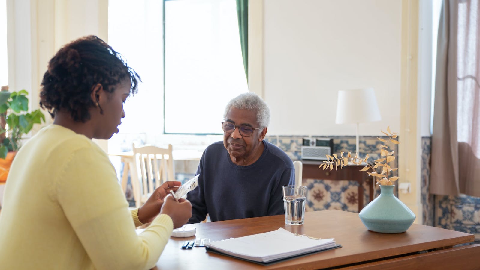 Younger woman at a table helping out an elderly man