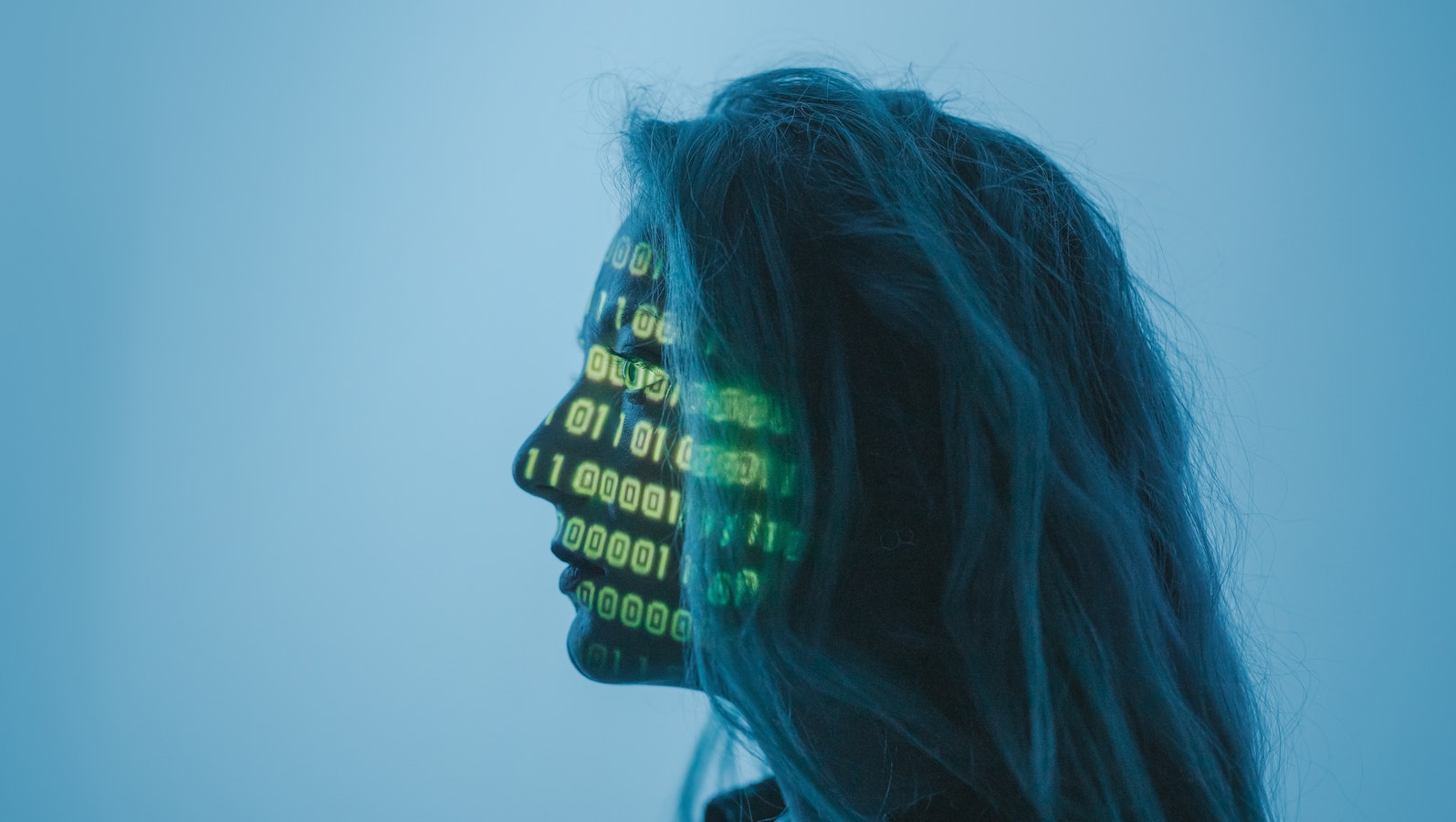 Side profile of a woman against a blue backdrop with binary code lit up across her face