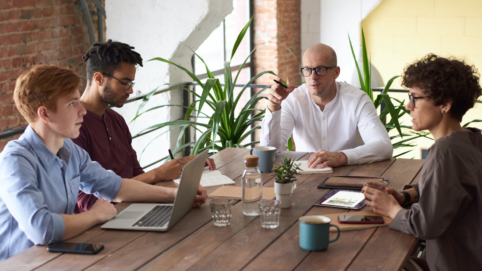 Four people sitting around a desk on laptops and talking