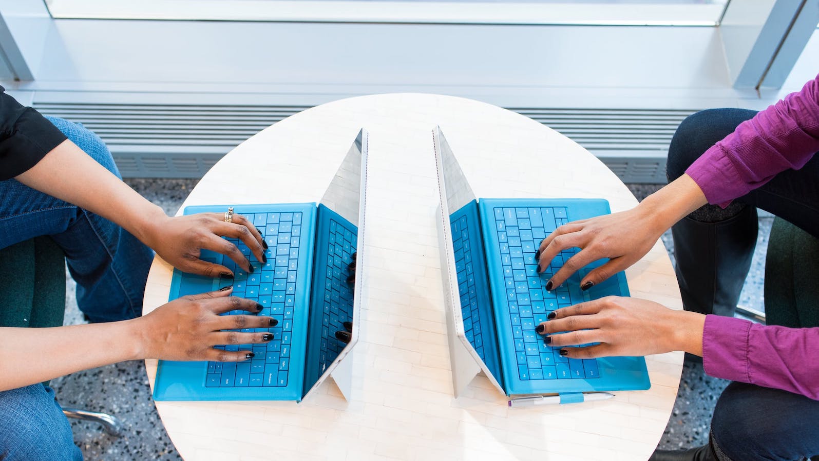 Two people sitting at a table facing each other while typing on laptops