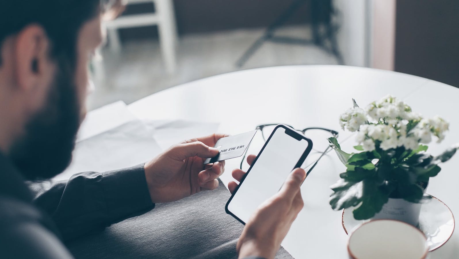 Man sitting at a table with his smartphone in one hand and a credit card in the other hand