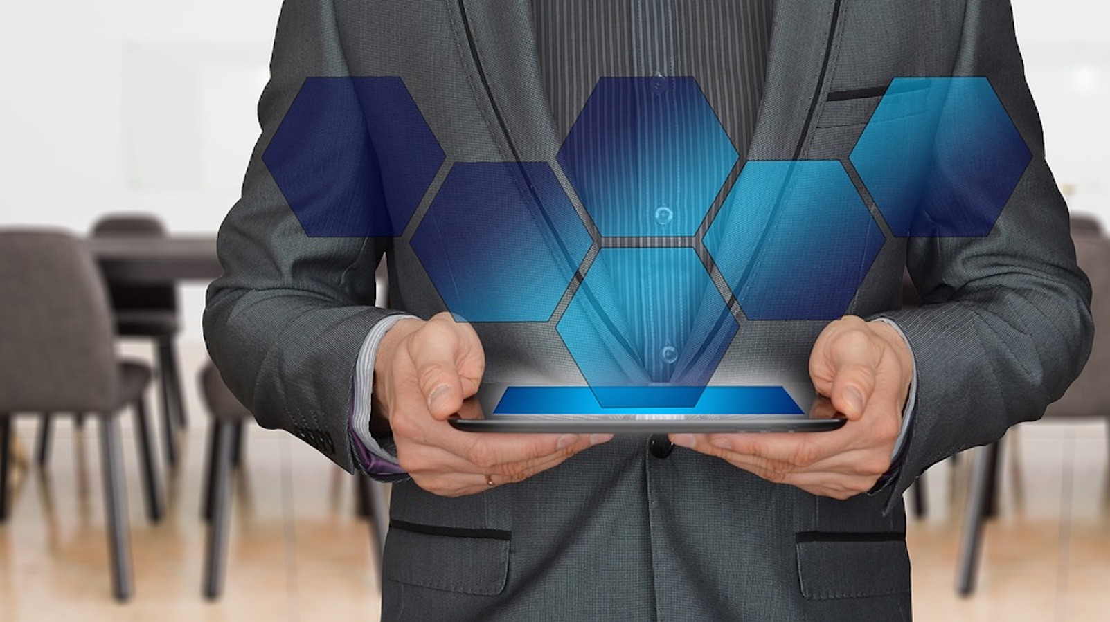 A person holding a tablet with holographic blue hexagons coming out of it