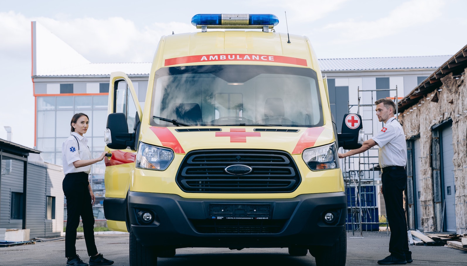 Man and woman standing on either side of a yellow and red ambulance outdoors