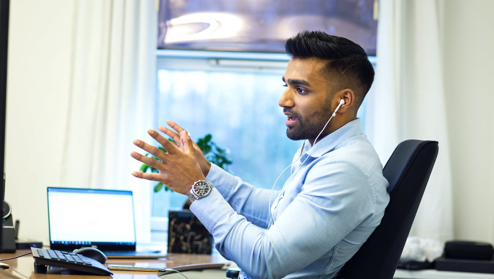 A person sitting at an office desk using hand gestures while talking to someone