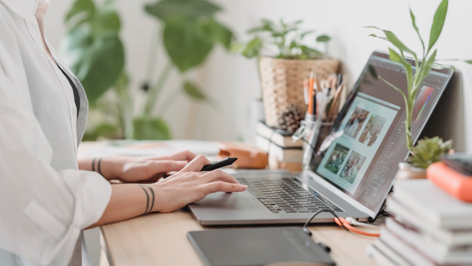 Person at a desk with a laptop open and plants and books on the desk