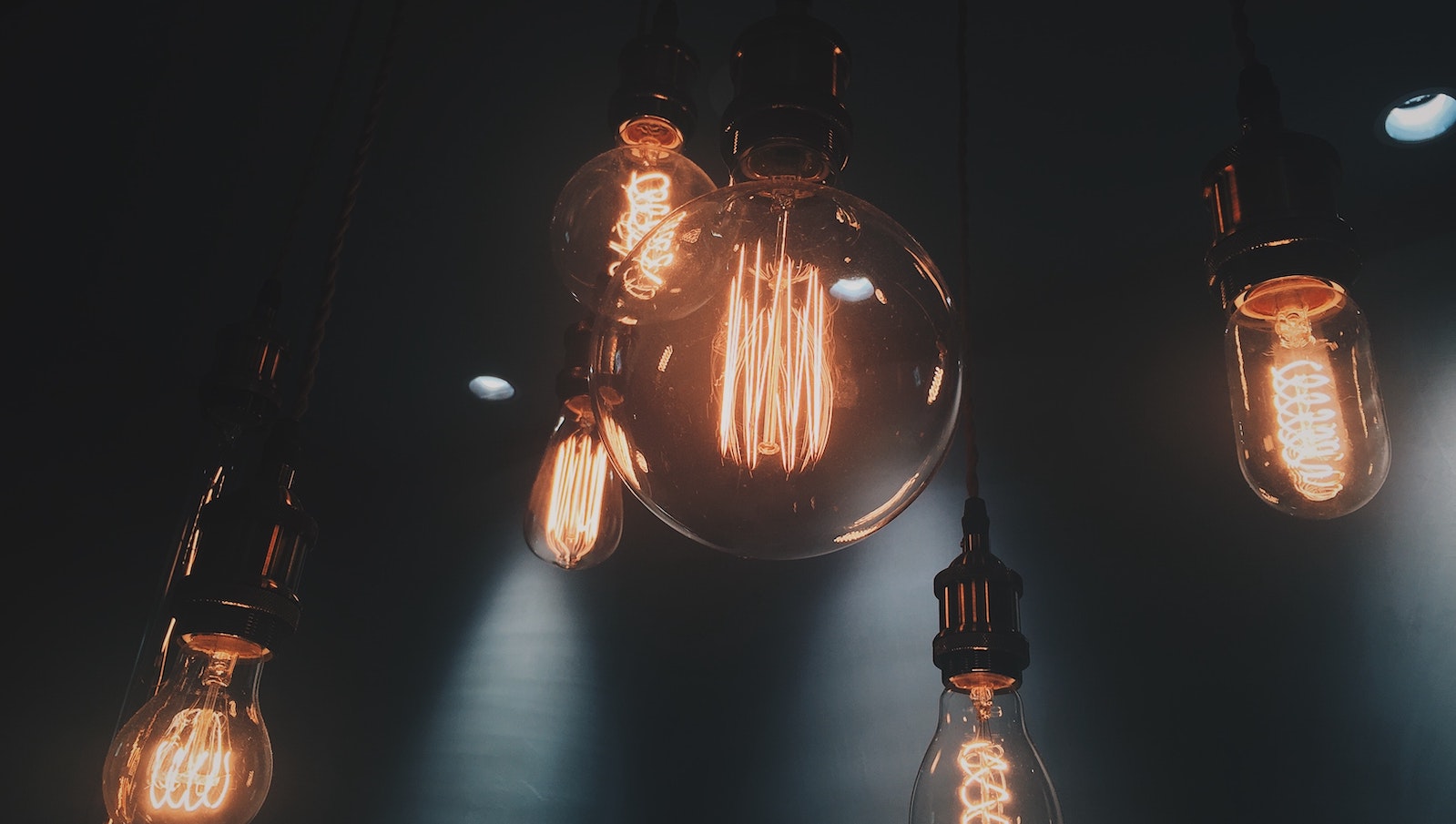 Six light bulbs of various sizes hanging from a ceiling and lit up