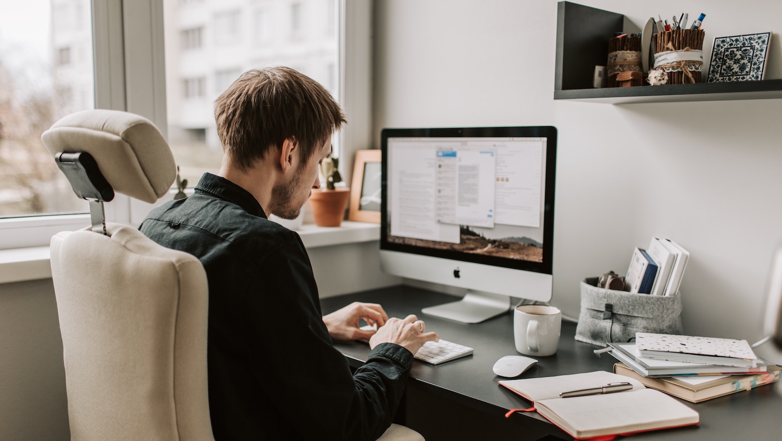 A man sitting at a desk typing on a Mac desktop computer