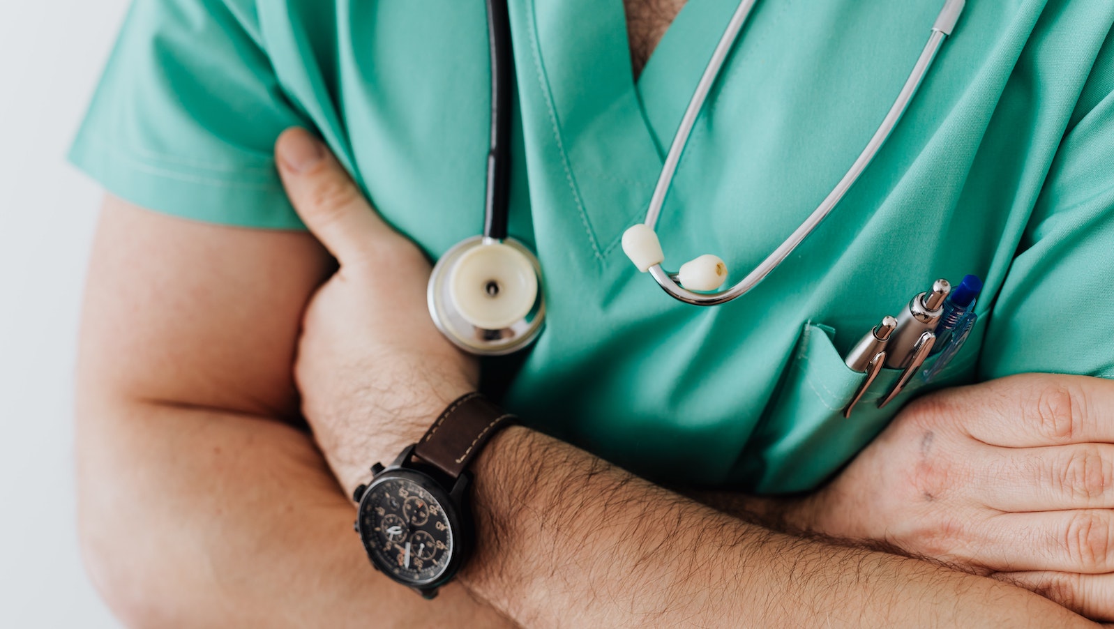 Man in green scrubs wearing a watch and crossing his arms also with a stethoscope around his neck