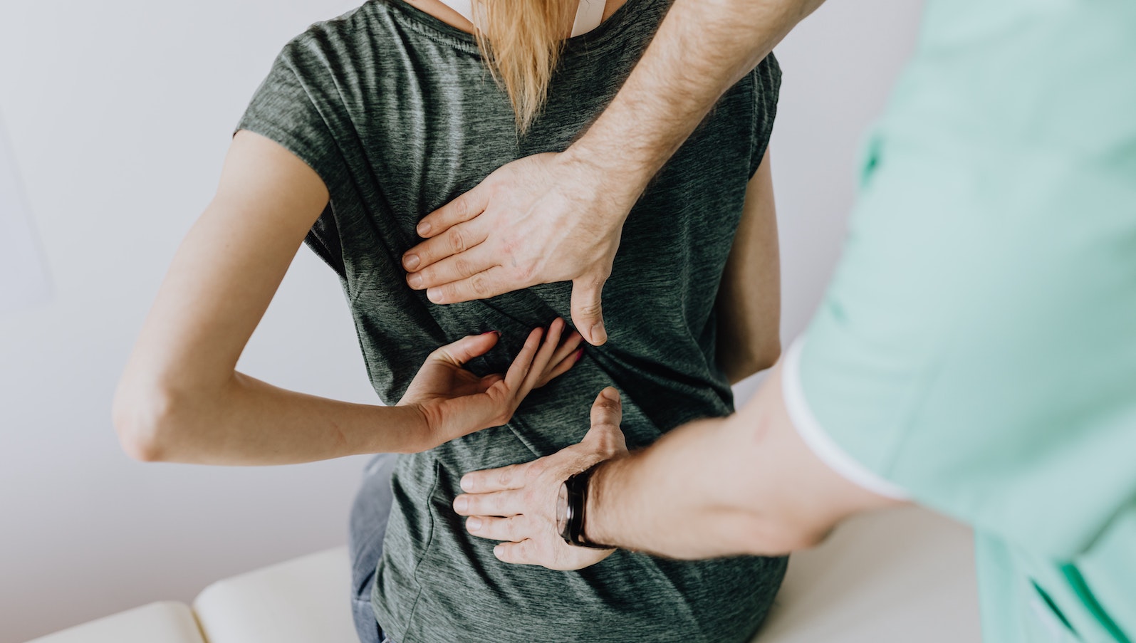 A doctor in green scrubs touching a patient's back while she shows him where the spot hurts