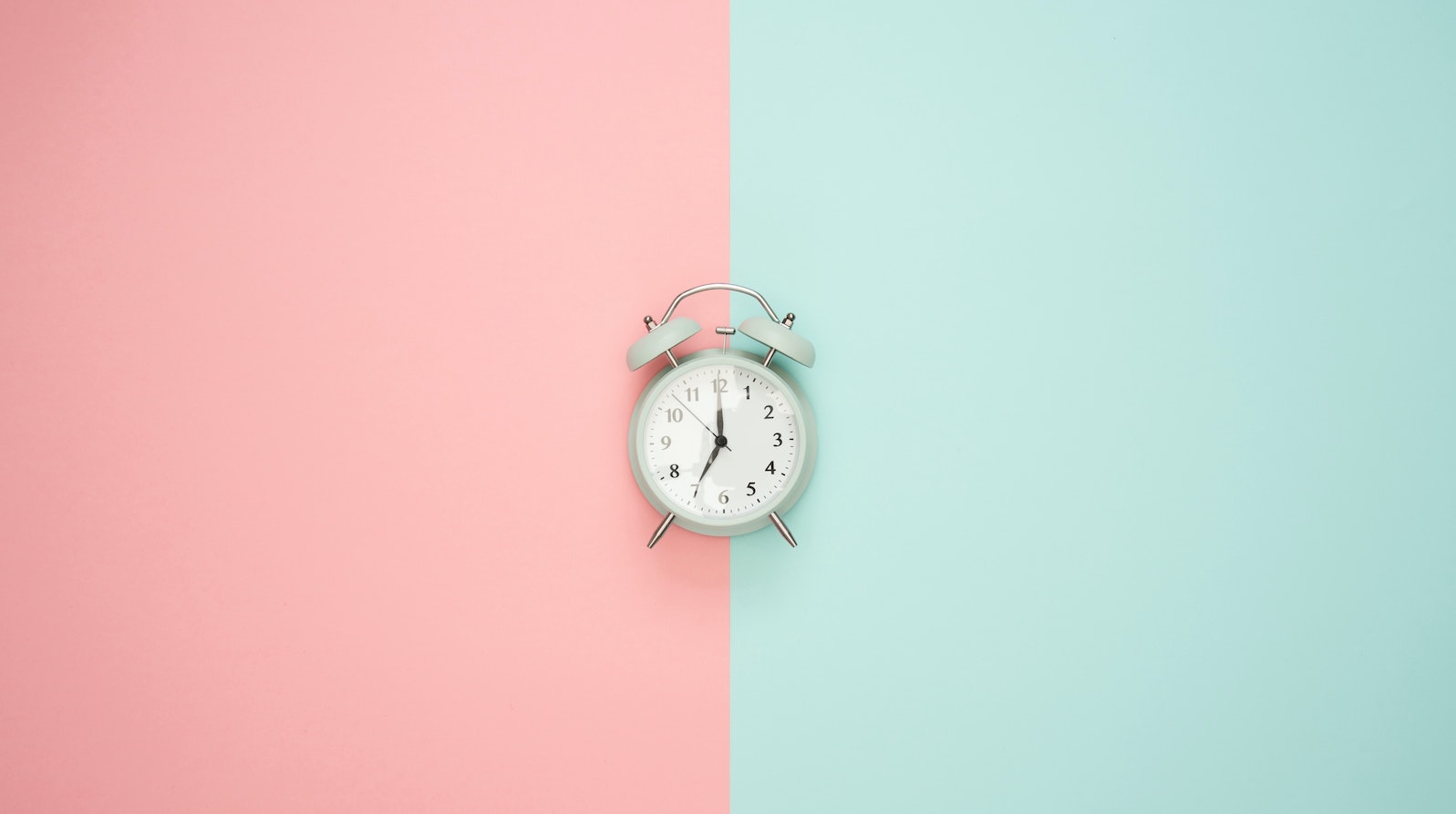 An analog clock set to seven o'clock against a half pink and half blue background