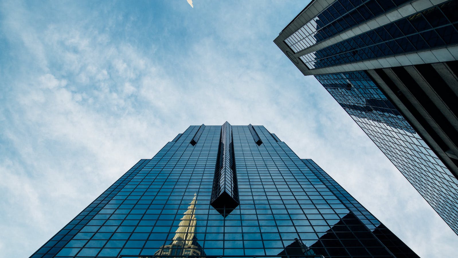 low-angle image of a tall glass building under a blue and cloudy sky