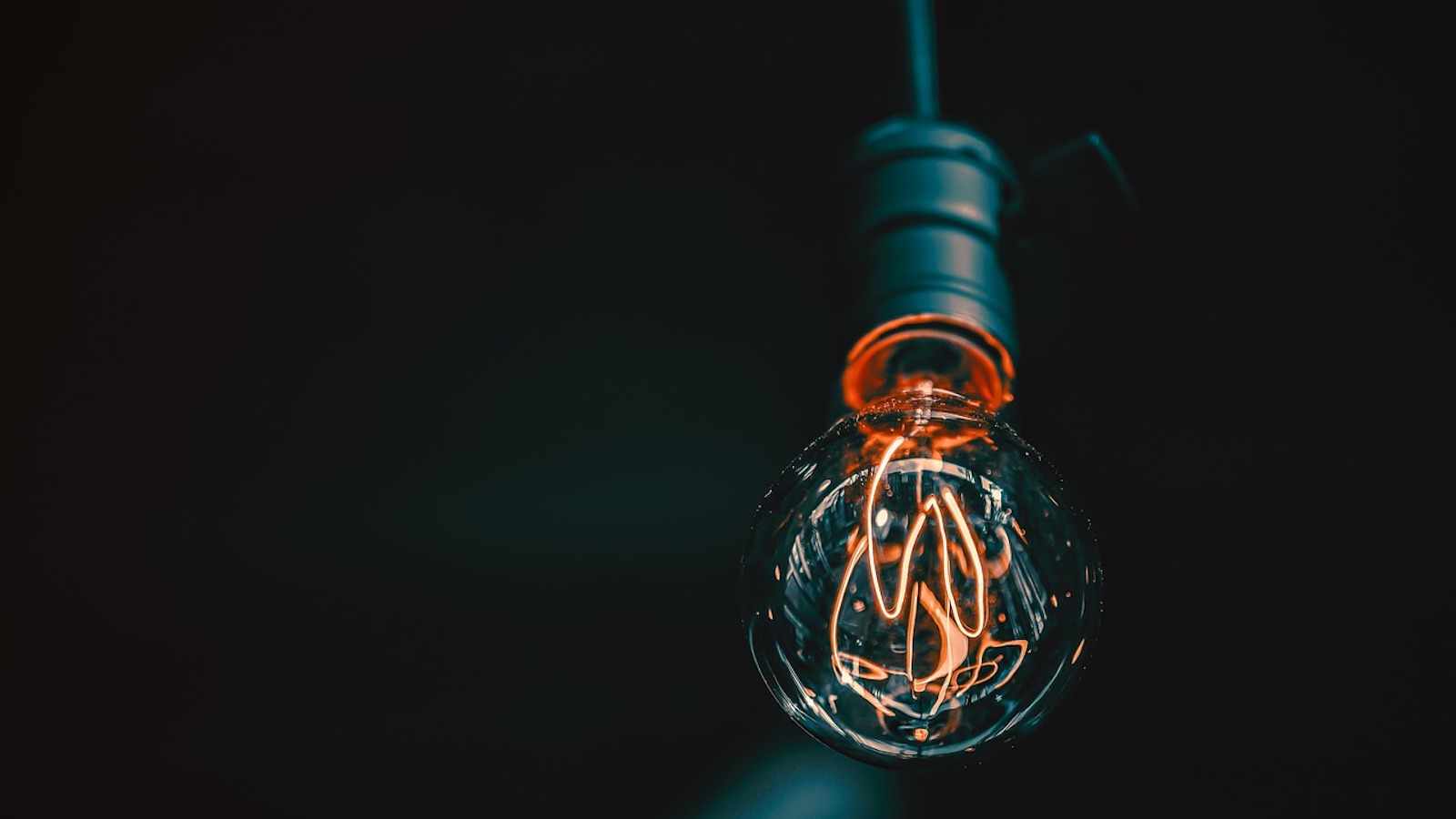 A lit-up lightbulb hanging from the ceiling against a black background