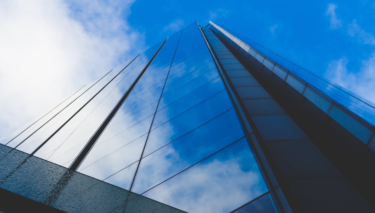 Low angle photo of a tall glass building against a blue sky that's reflective