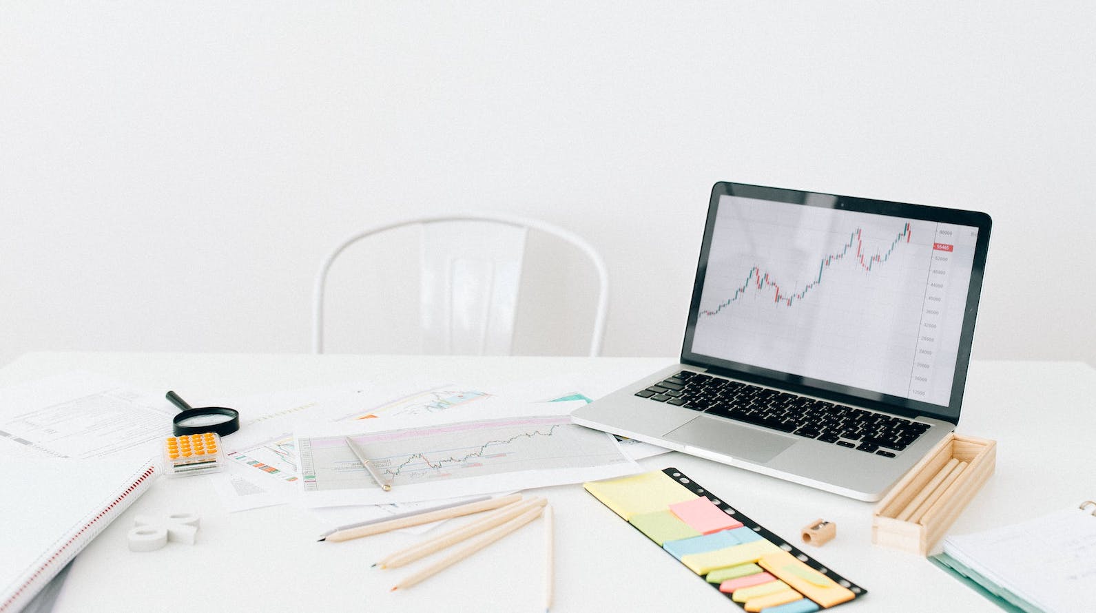 A Laptop Near Documents and Post it Paper on a White Table