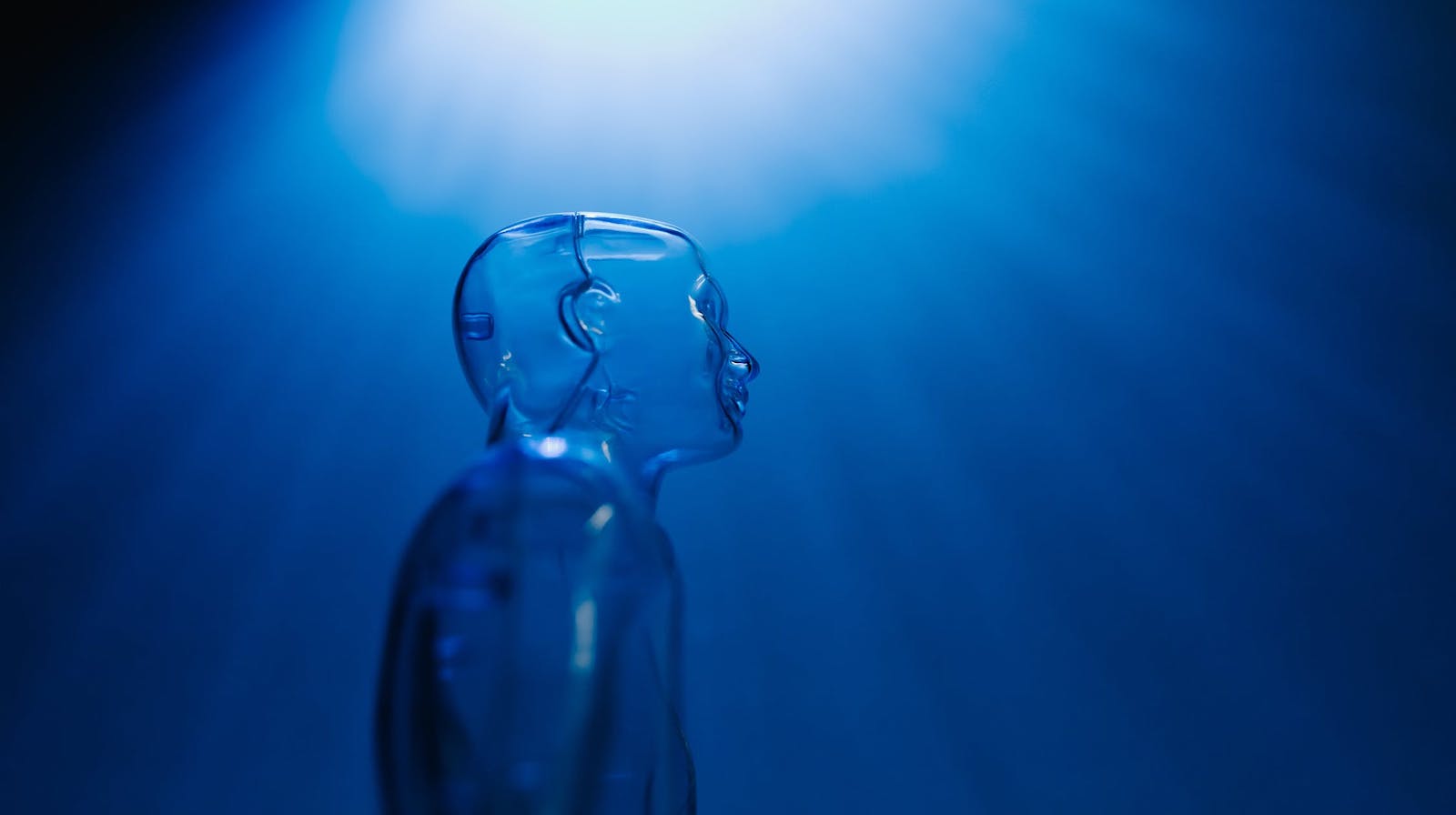 A clear mannequin against a dark blue background with light emanating from the top