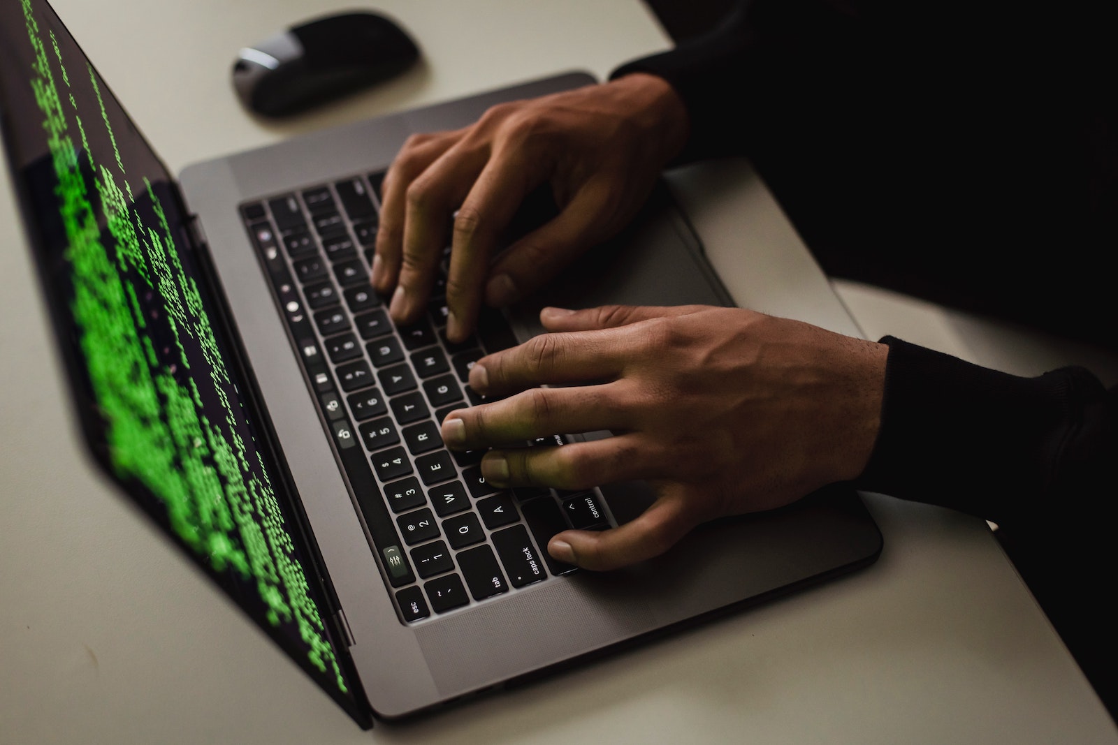 Close-up of hands typing on a computer with neon green words on the screen