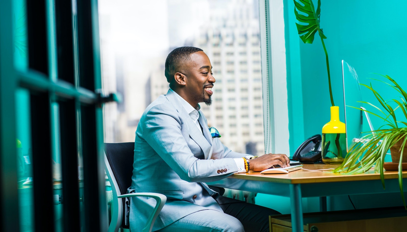 Man sitting at a desk smiling and in front of a teal background