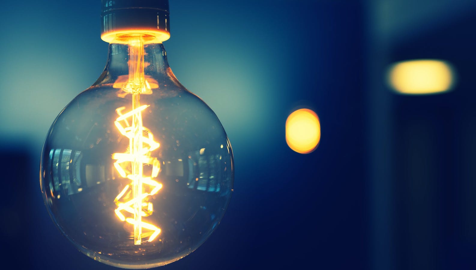 A light bulb hanging from the ceiling lit up against a dark background 