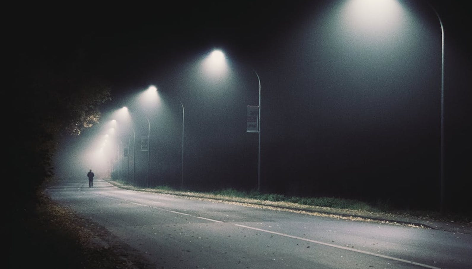 A person walking on a dark road with spotlights along the road