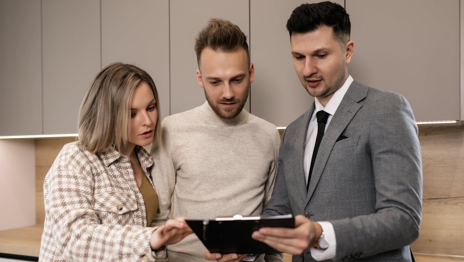 Three people standing all huddled around and looking at a tablet