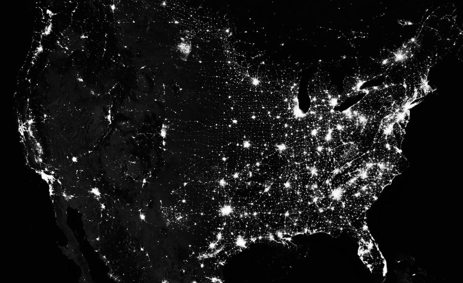 A map of the US displayed by lights in particular clusters around big cities all set against a pitch black background