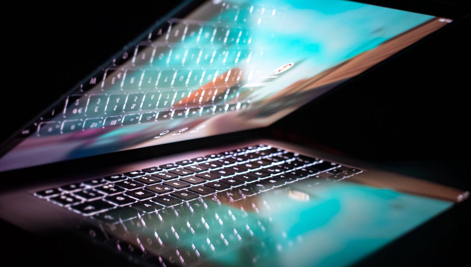 Partially closed laptop showing a turquoise glare